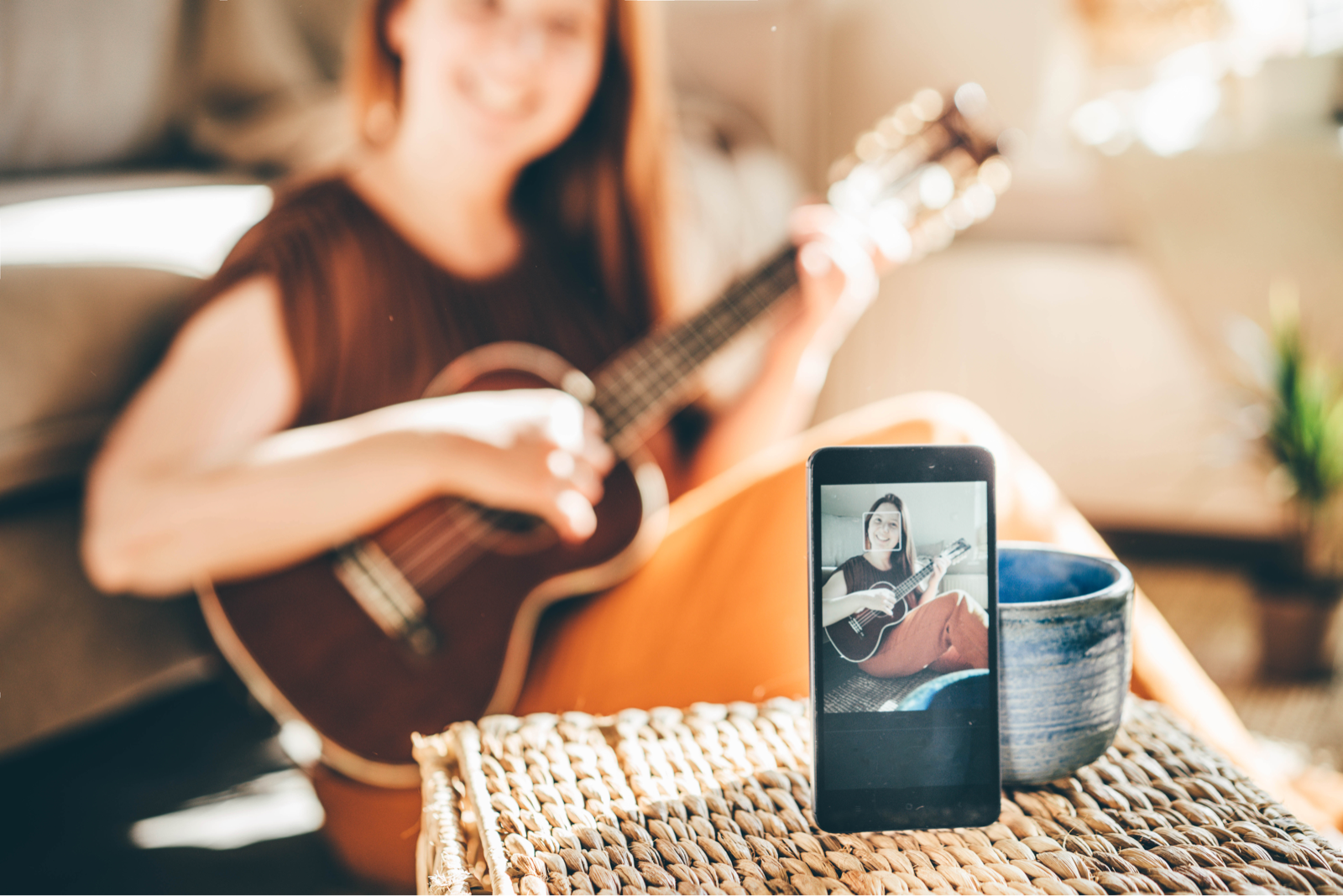 カップにスマートフォンを立てかけて、ギター演奏を動画撮影する女性