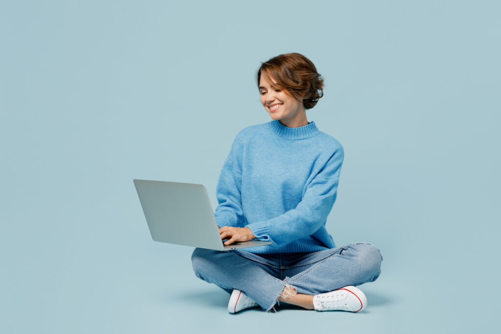 青いニットを着てパソコンを触る女性