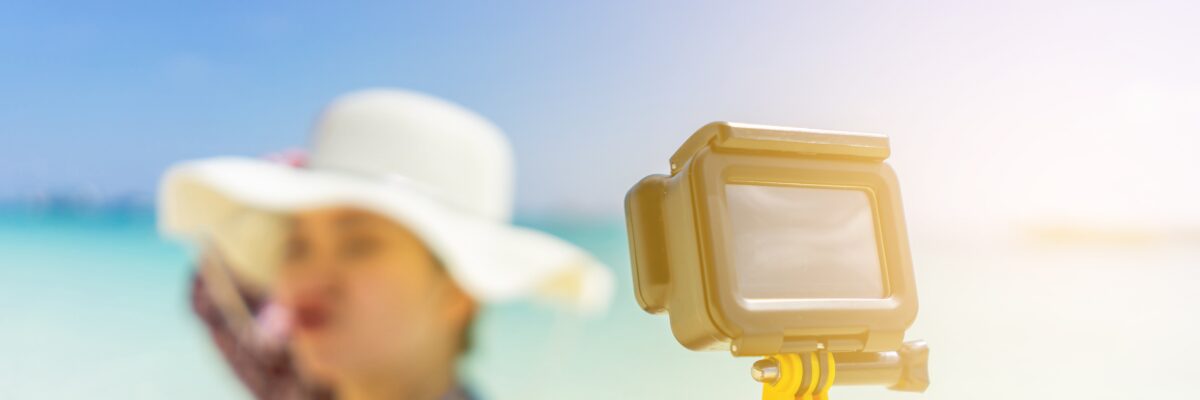 帽子をかぶった女性が海辺でカメラを持って撮影している