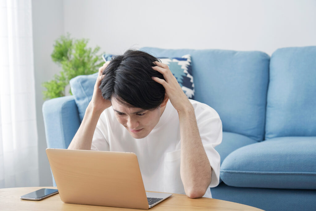 青いソファの前でパソコンを見て頭を抱える男性
