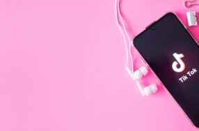 ピンクの背景にTikTokの画面が写っているスマートフォンとイヤホン